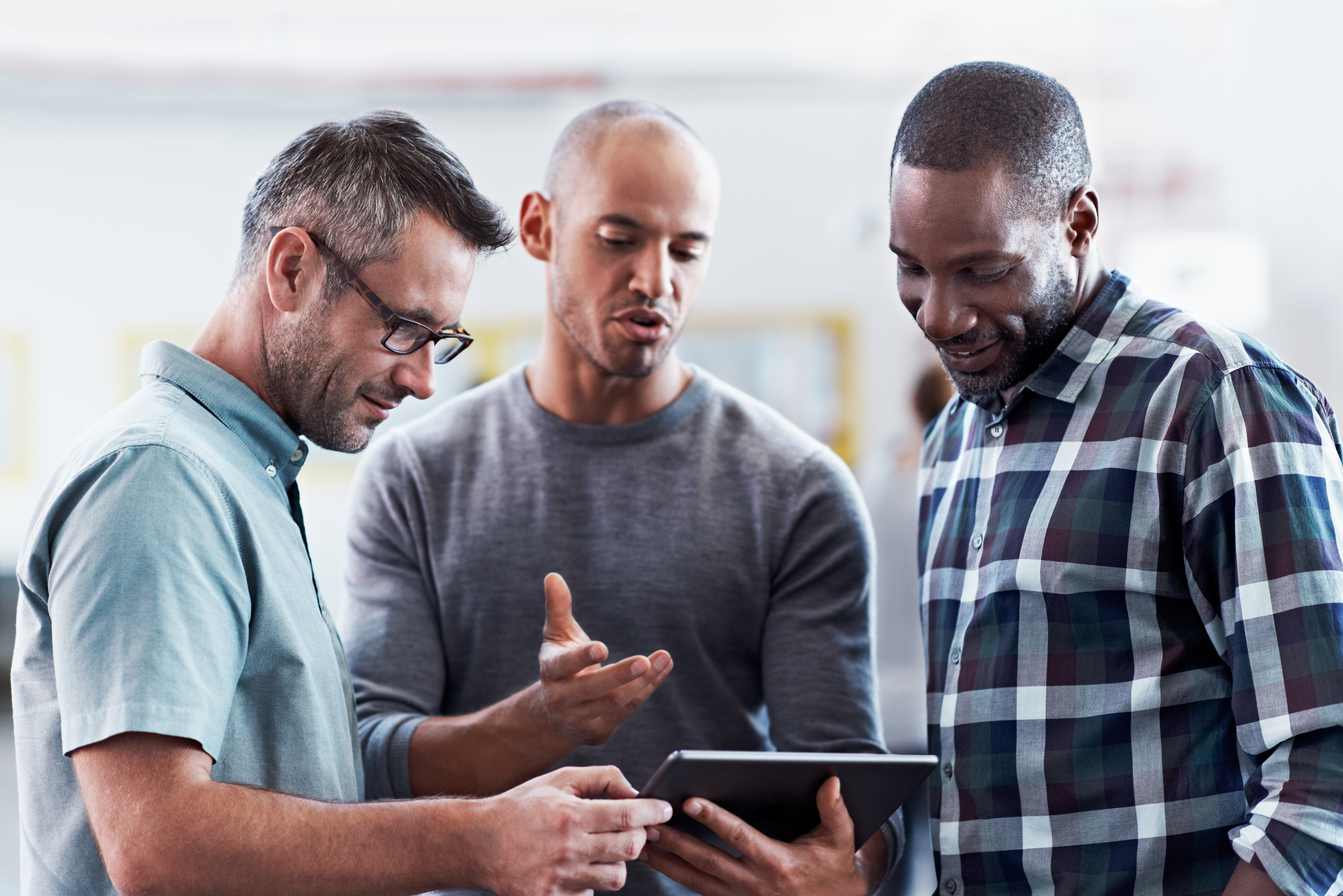 Three people standing together discussing something, while looking at a tablet.
